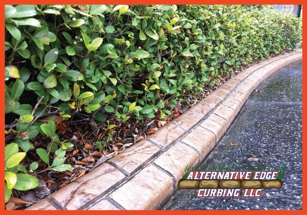 Curved concrete curbing with a brick pattern edging a garden bed and road; 