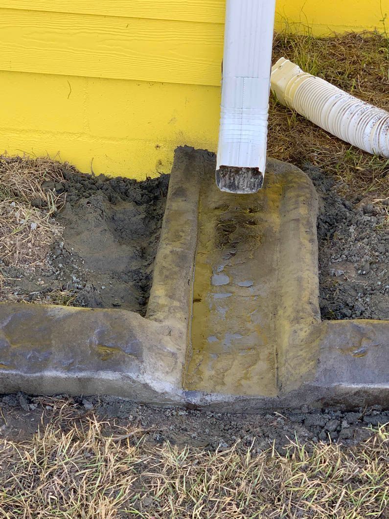 Concrete foundation with downspout, stained with water damage and dirt.