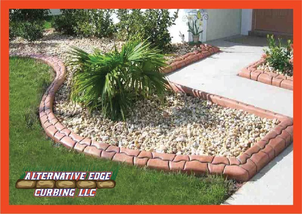 Concrete landscaping curbing with reddish-brown stones edging a garden filled with rocks and plants; grass and walkway visible.