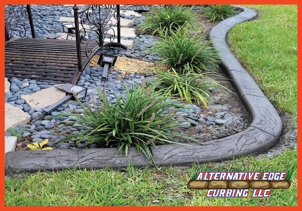 Concrete curbing separates a lawn from a garden bed filled with greenery, rocks, and stepping stones.