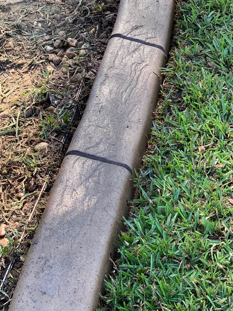 Concrete landscape edging separating grass and dirt.