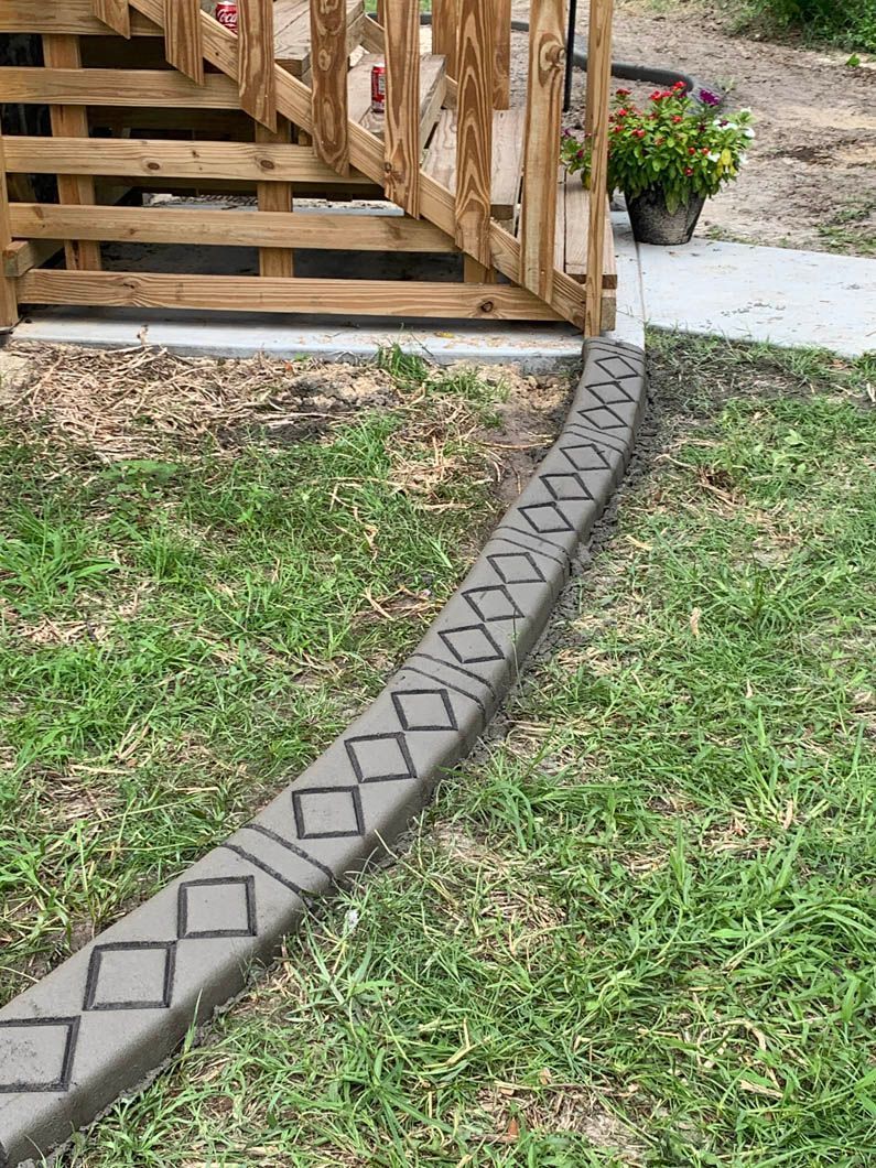 Concrete border with diamond design along a grassy lawn, near a wooden staircase and flowers.