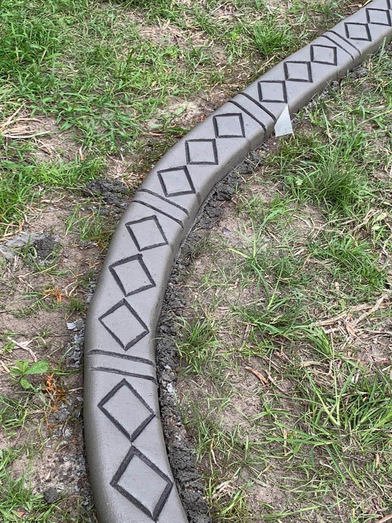 Curved concrete garden edging with black diamond and line patterns on grass.
