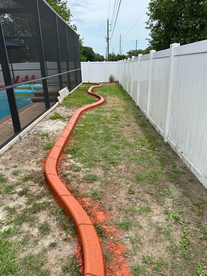 Orange landscaping border snakes along a patch of grass beside a white fence and screened pool enclosure.