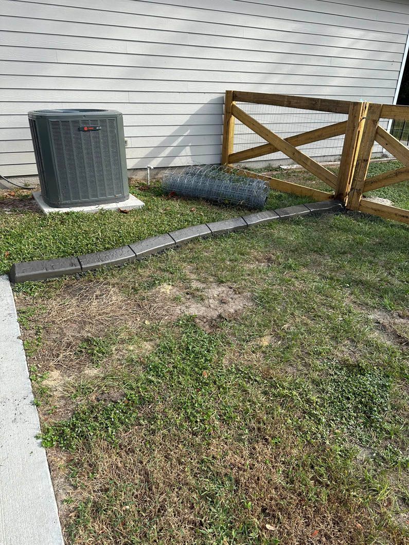 Air conditioner, fence, and rolled-up wire on grass next to a building.