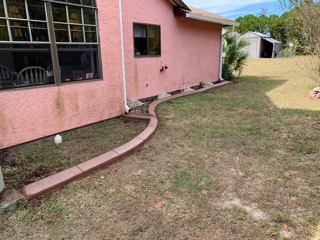 Pink stucco house with brown curbing, a window, and dry grass.