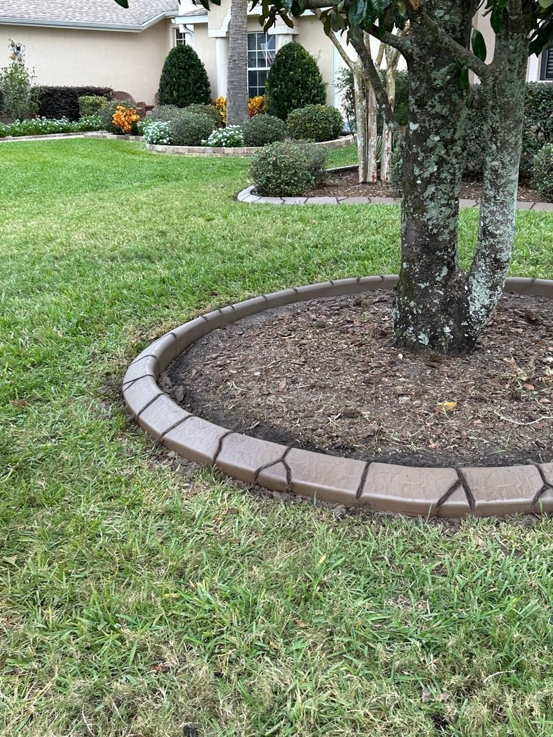 Brown stone edging around a tree in a grassy yard.