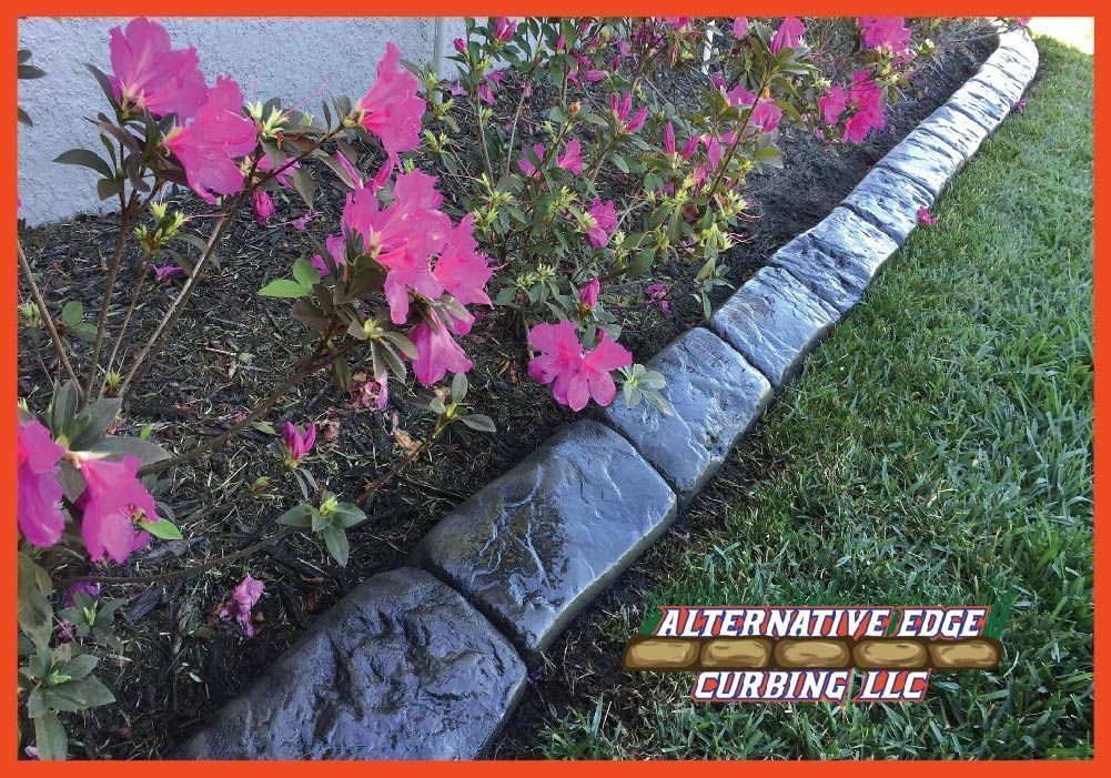 Concrete curbing edging a garden bed with pink flowers and green grass.