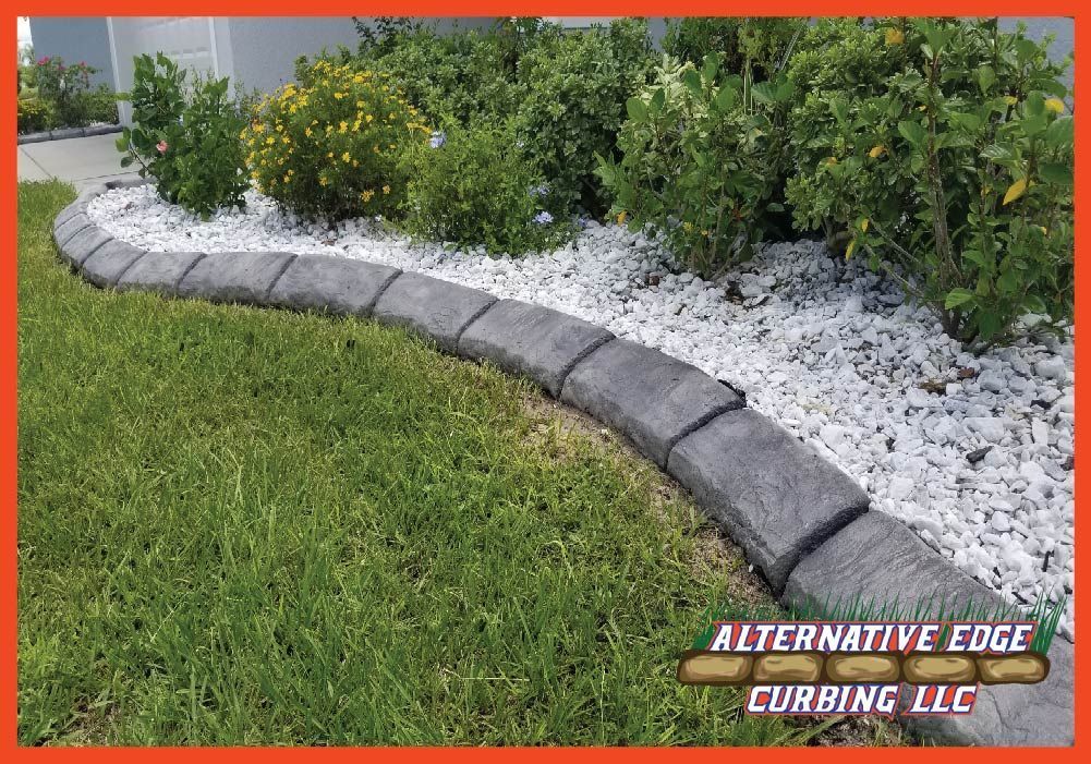 Gray concrete curbing separating green lawn from white-rock flower bed with bushes.