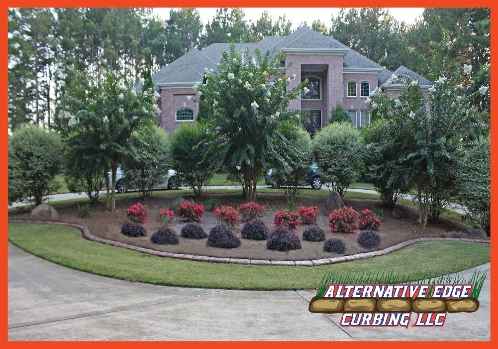 Manicured landscape with a variety of bushes and flowers in front of a brick house with a curved driveway.