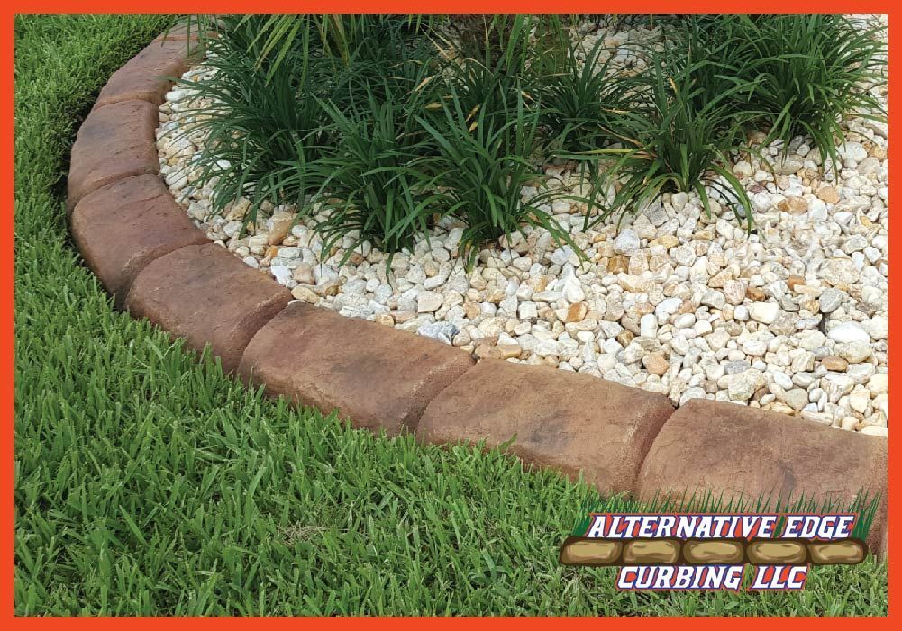 Brown concrete curbing edging a garden bed filled with pebbles and plants, surrounded by green grass.