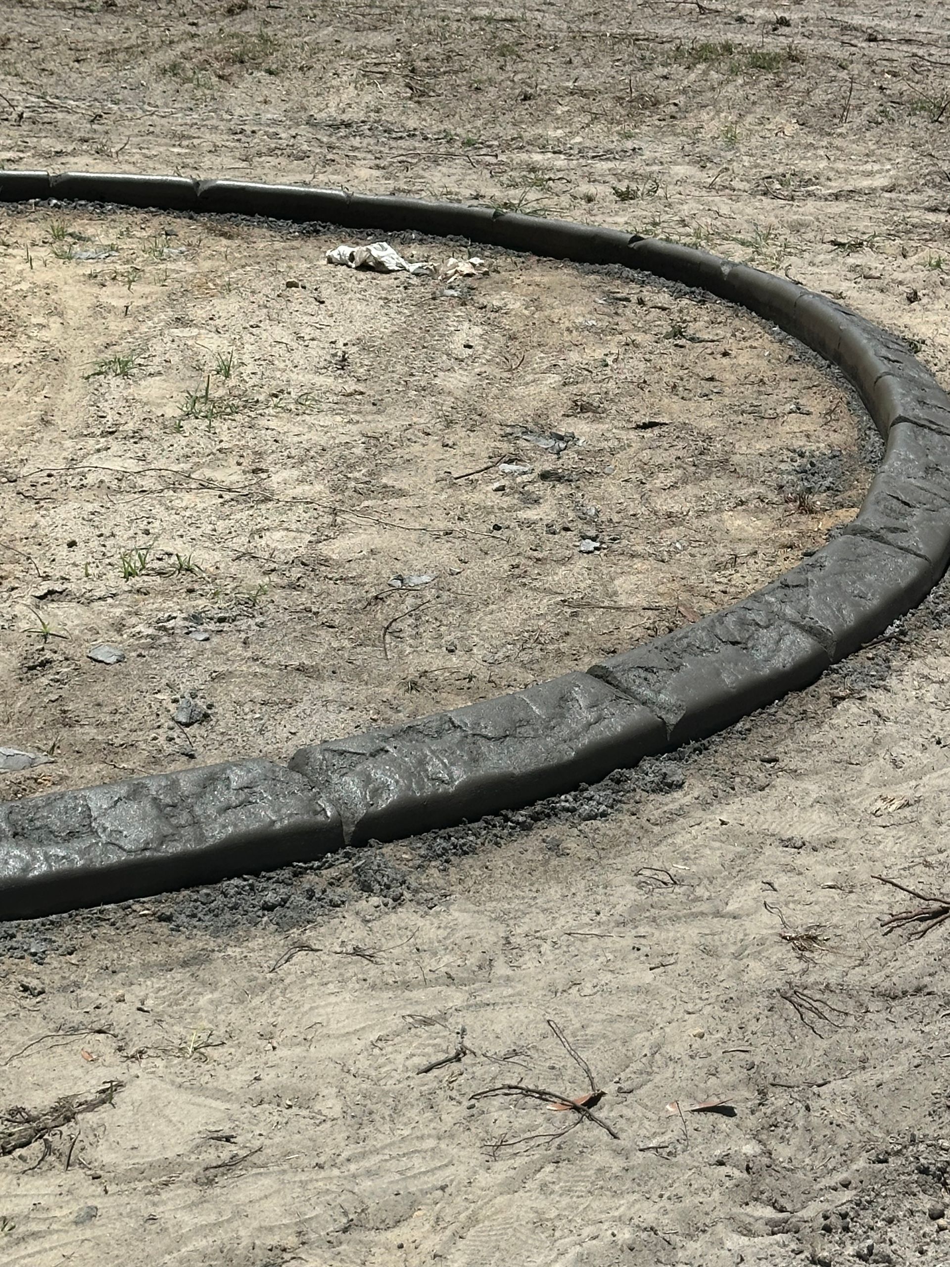 Curved, dark gray concrete edging bordering a sandy area.