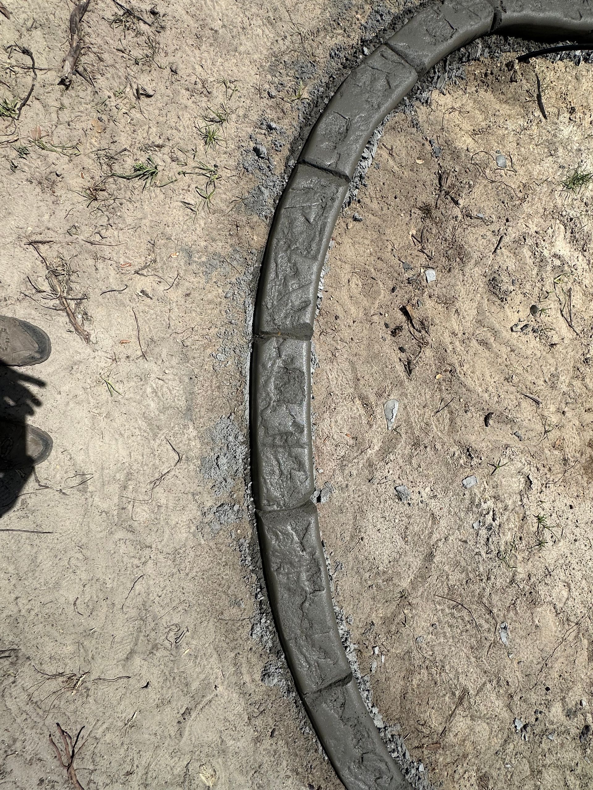 Curved concrete border on dirt ground, forming a circular edge.