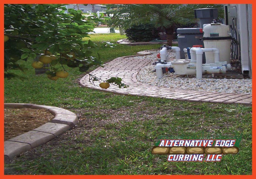 Brick curbing around a yard with green grass and a pool pump area.