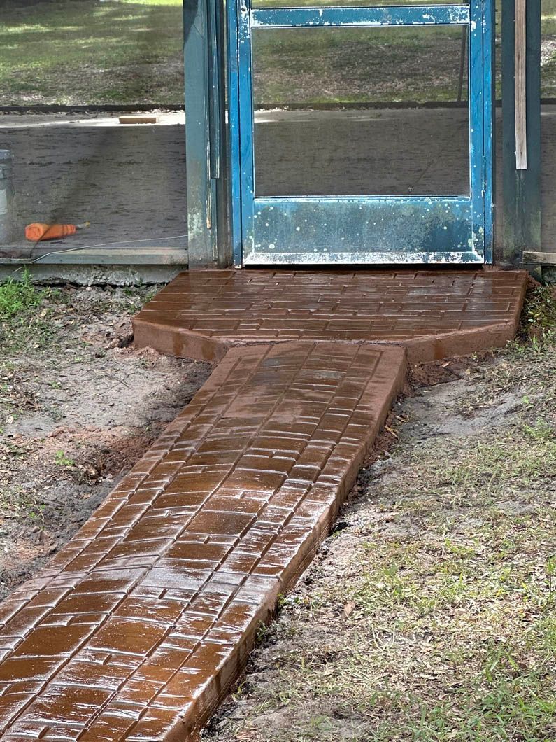 Brick-patterned walkway leads to blue screen door on wooden structure. Brown and green colors prevail.