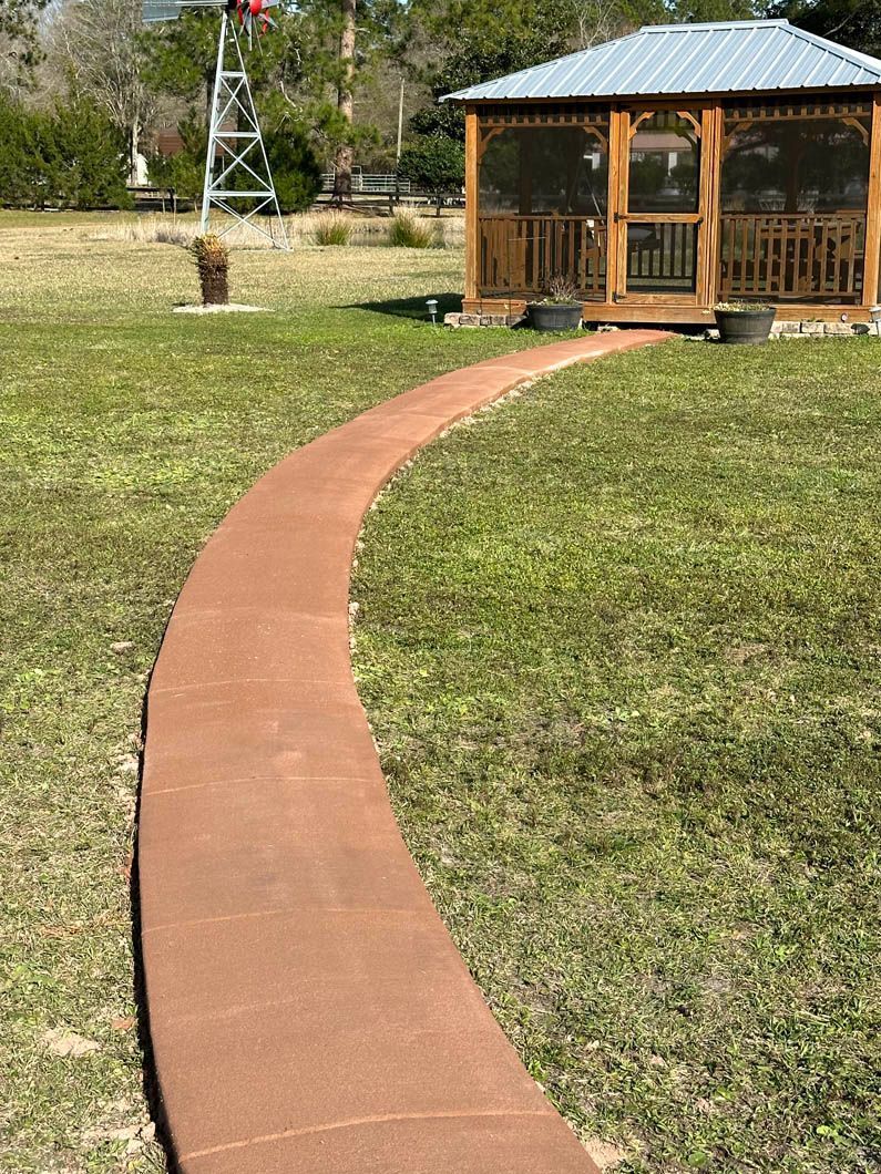 Curving red-brown pathway leads to a wooden gazebo in a grassy yard, windmill in the background.