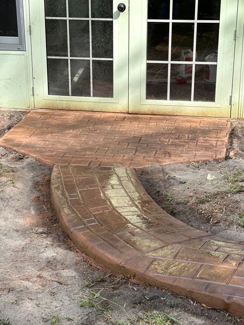 Brick-patterned walkway leads to a glass-paned door. Brown and tan colors, outdoor setting.