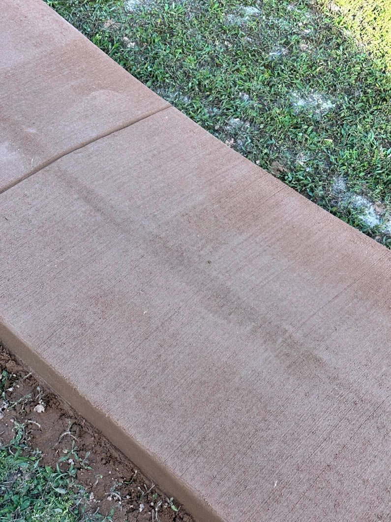 Brown concrete sidewalk with grass in the background, with two rectangular sections and a slight texture.