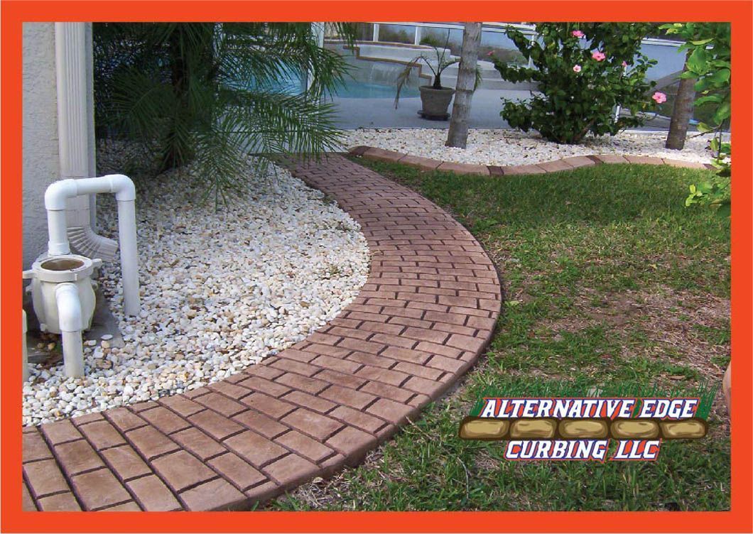 Curved brick pathway with grass and white stone landscaping. Orange framed logo on right.