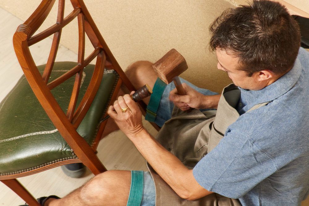 A Man Is Working On A Chair With A Hammer — Coastal Upholstery In Berkeley Vale, NSW