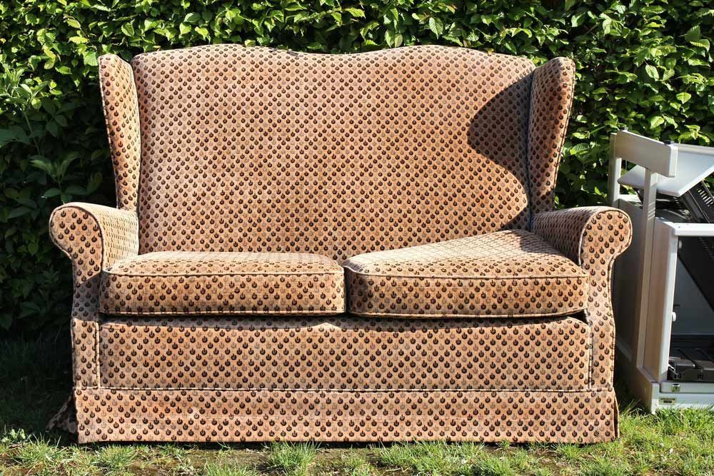 A Brown Couch Is Sitting In The Grass Next To A White Chair — Coastal Upholstery In Berkeley Vale, NSW