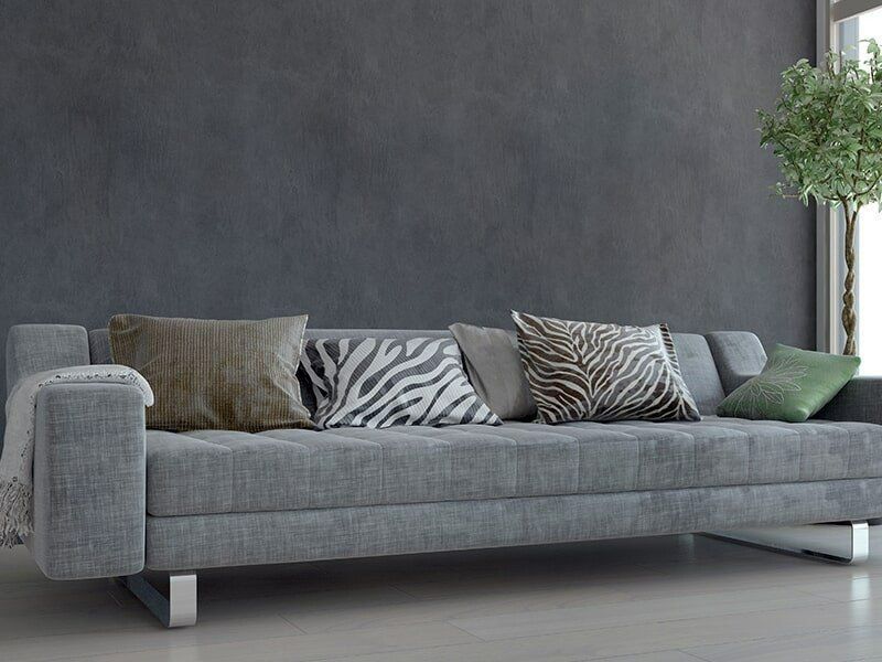 A Grey Couch With Zebra Print Pillows Is Sitting In A Living Room Next To A Window — Coastal Upholstery In Berkeley Vale, NSW