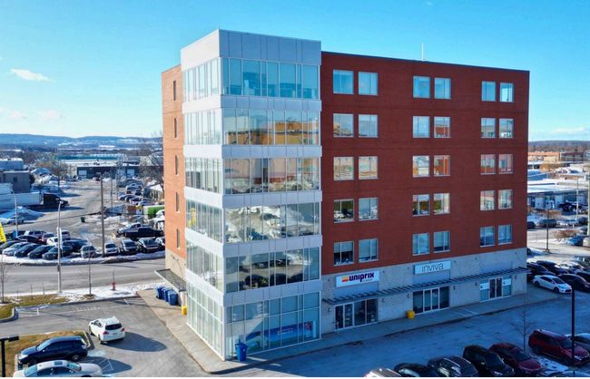Un immeuble de bureaux moderne rouge et vitré avec des voitures garées dans une zone urbaine enneigée