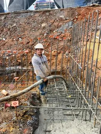 Construction worker pouring concrete at a construction site. He is wearing a hard hat, and standing in the concrete.