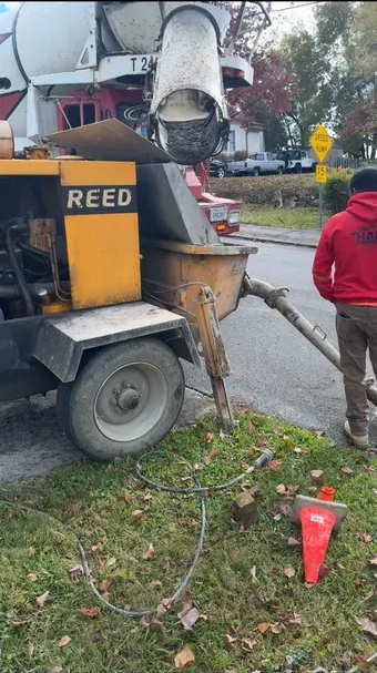 Concrete pump truck pouring concrete on a grassy area, with a worker standing nearby.