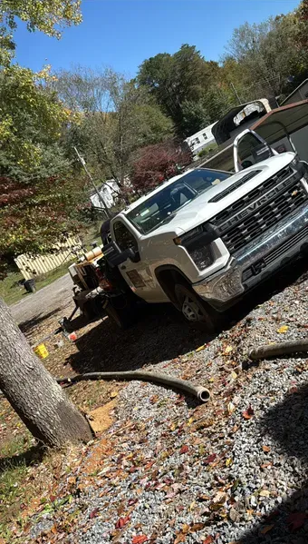 White pickup truck parked on gravel next to a tree, with an open door.