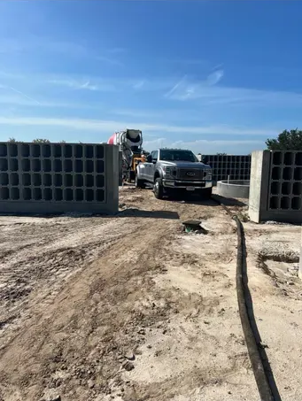 Concrete truck near gray block walls on a construction site under a blue sky.