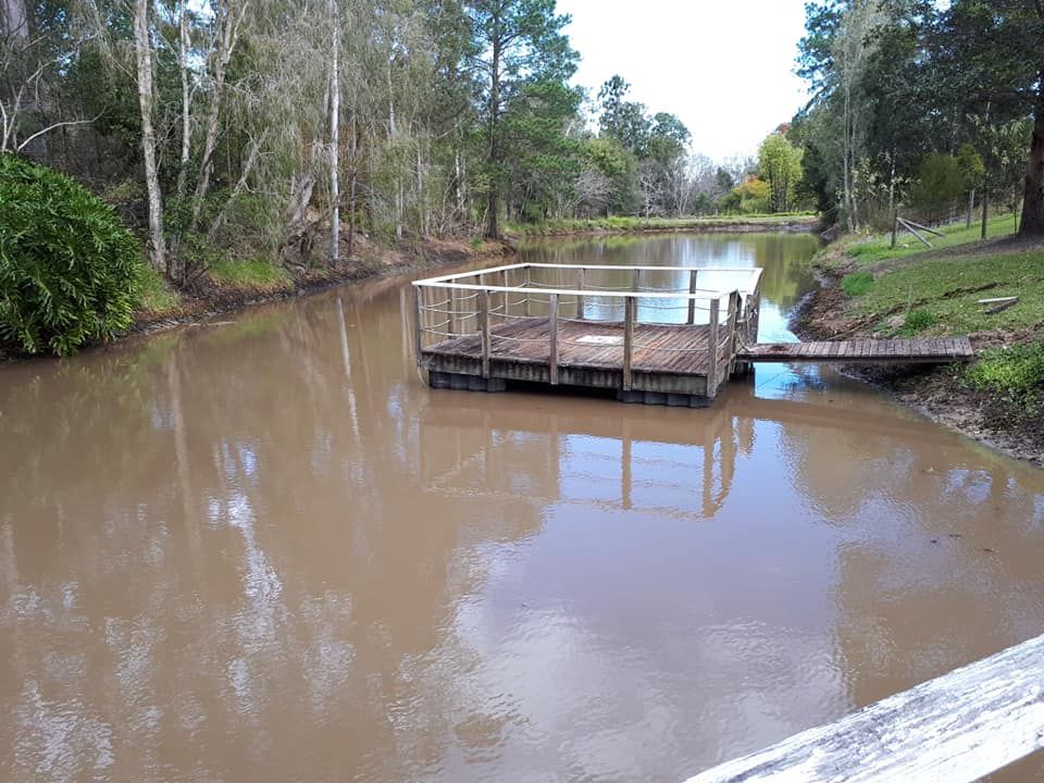 A Muddy River With A Wooden Dock In The Middle Of It — Dams Cleaned in Mudjimba, QLD