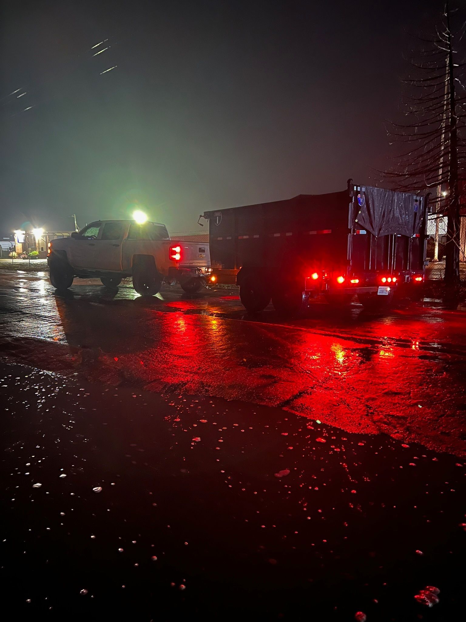 Trucks parked on wet pavement at night, with red taillights reflecting.