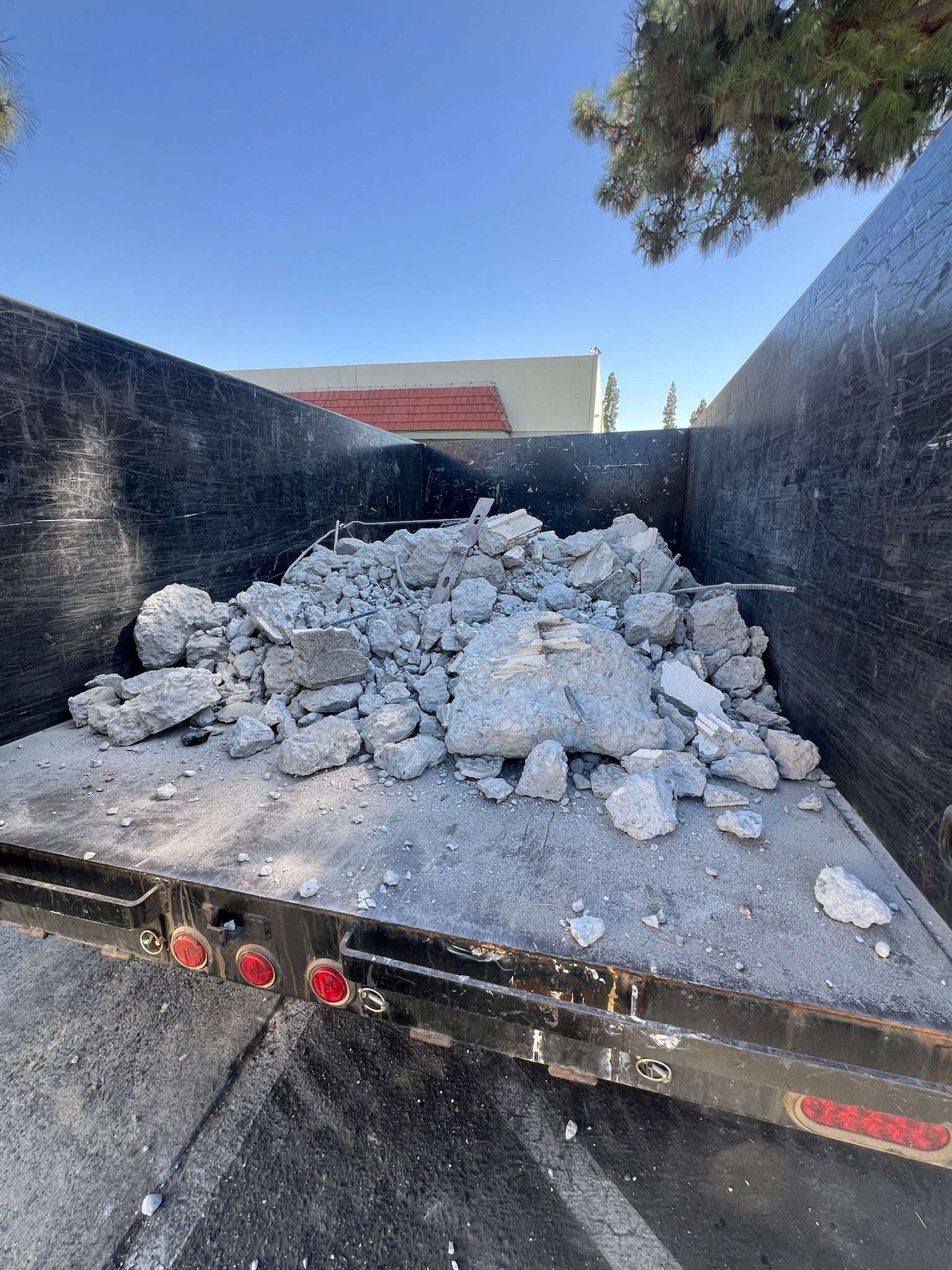 Dump truck bed filled with gray rubble, outdoors under a blue sky.