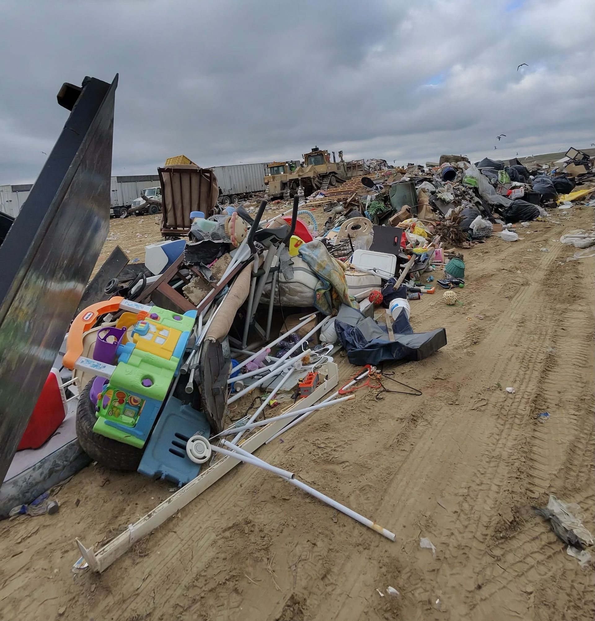 A large pile of trash and debris, including toys, furniture, and construction materials, in a landfill.