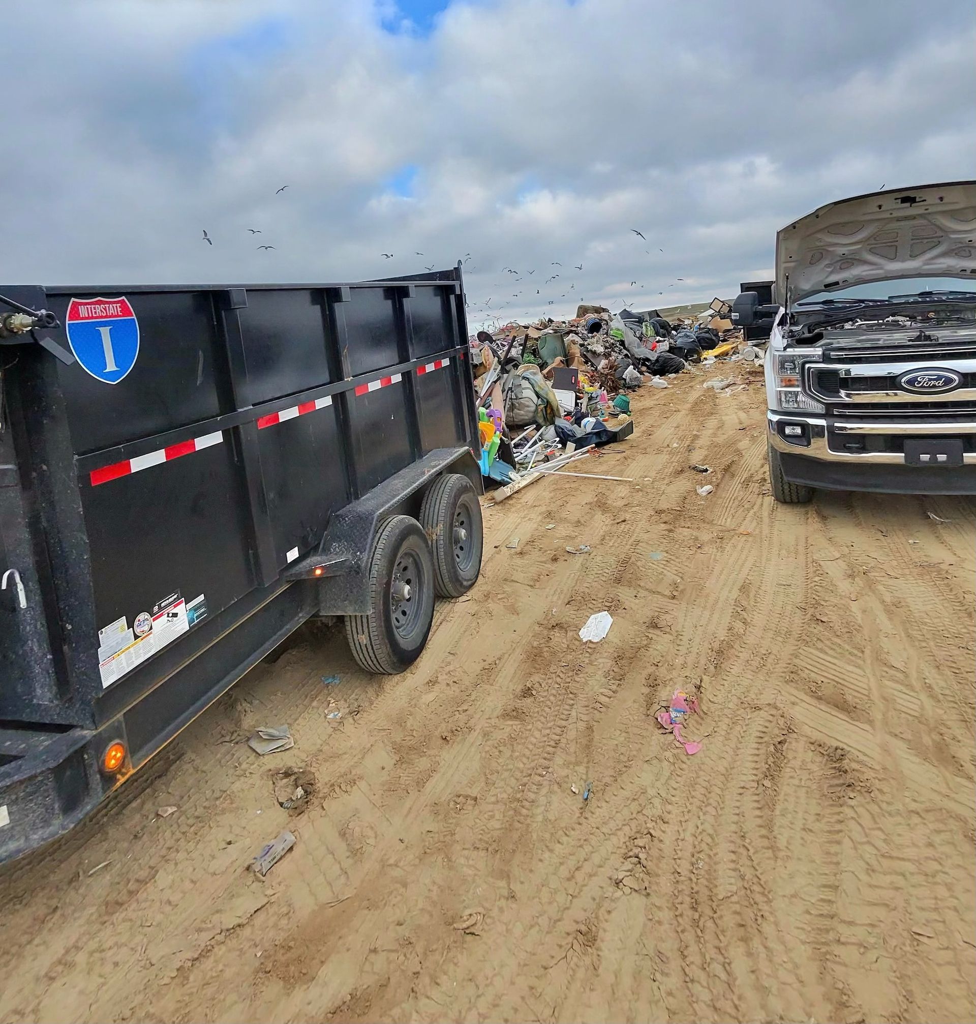 Black trailer and truck next to a large pile of trash at a landfill.