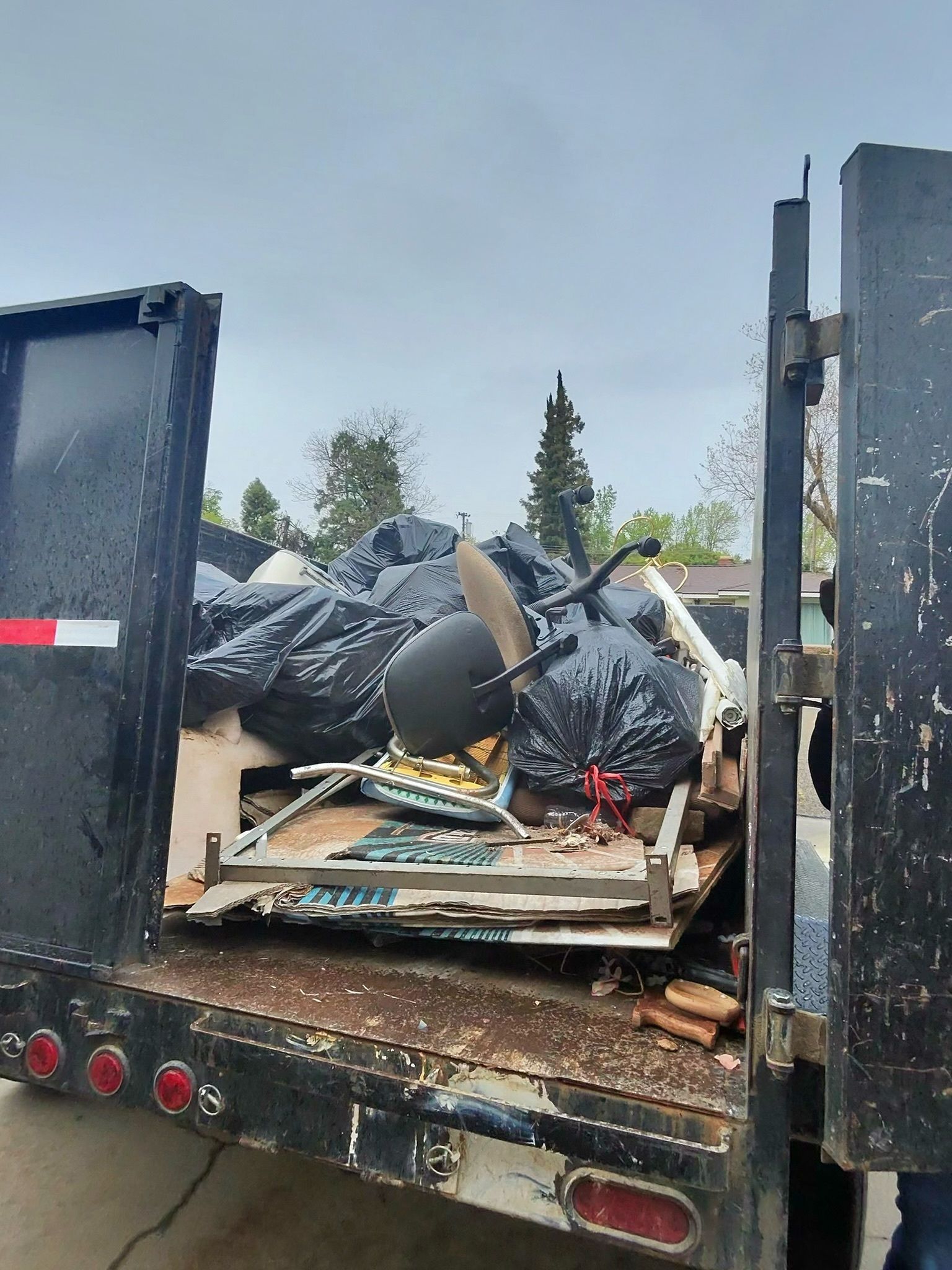 Dump truck bed overflowing with black trash bags and debris, parked outdoors.