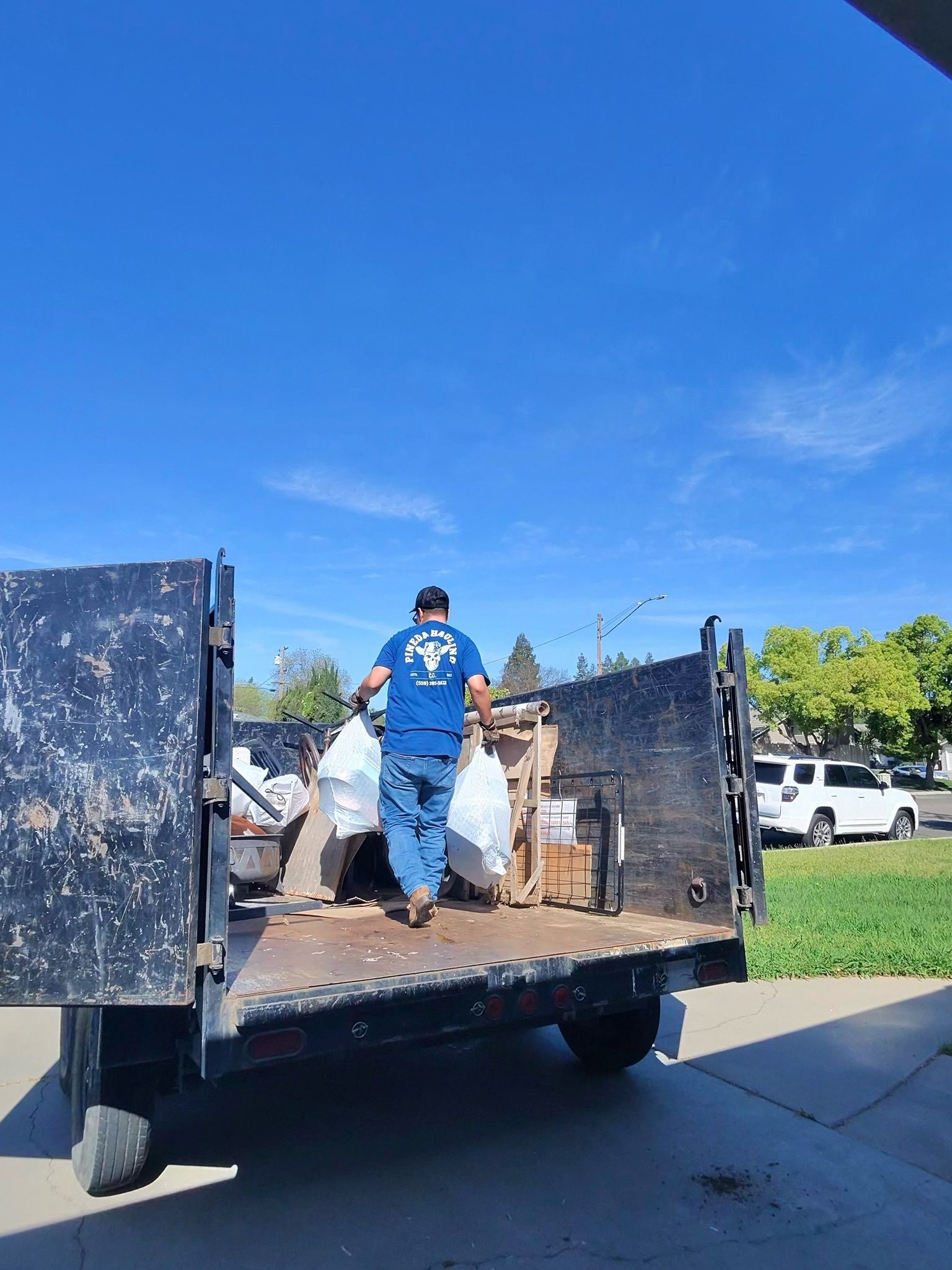 Man loading trash into a black truck on a sunny day.
