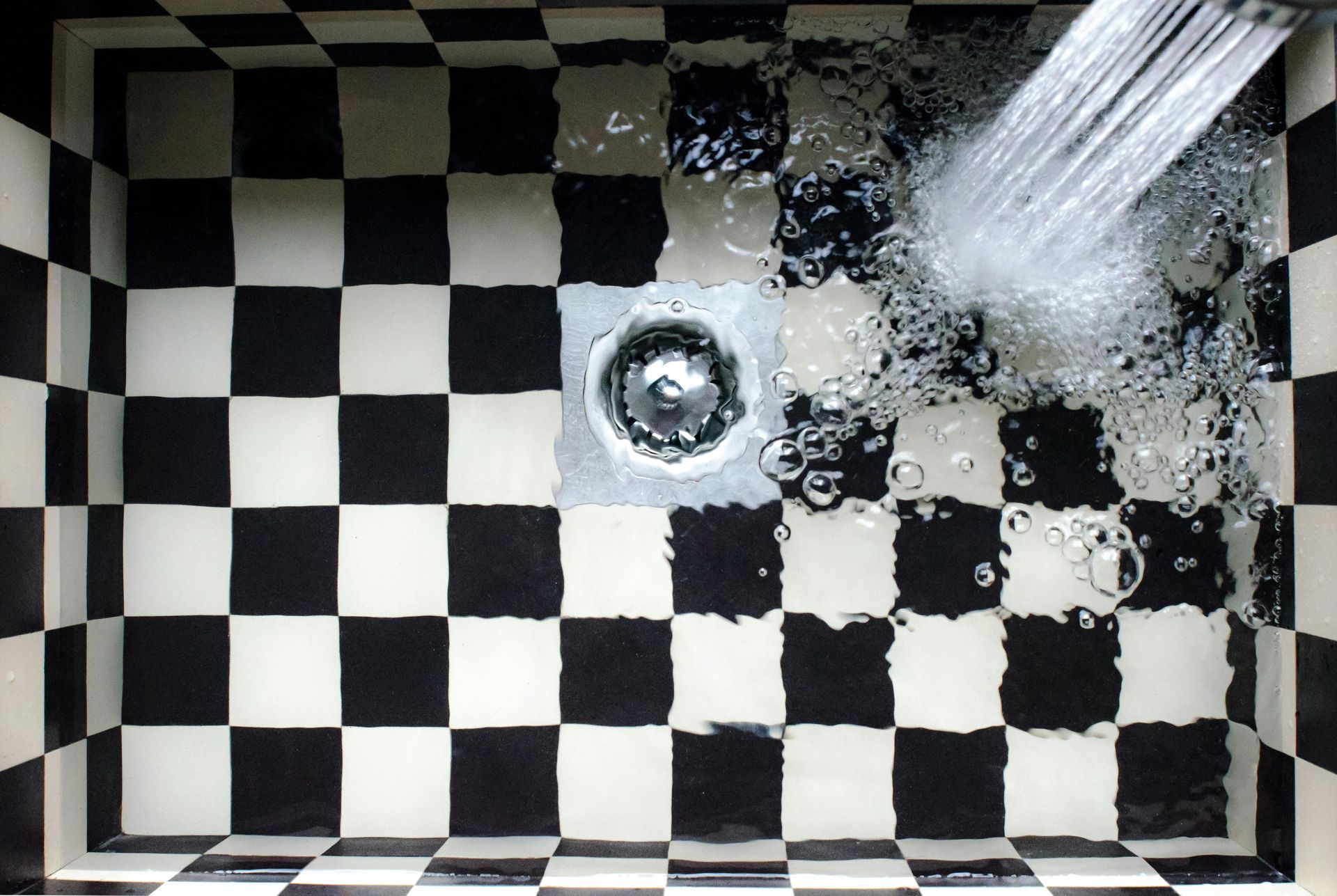 De l'eau s'écoule dans un lavabo à damier noir et blanc, la bonde étant visible.