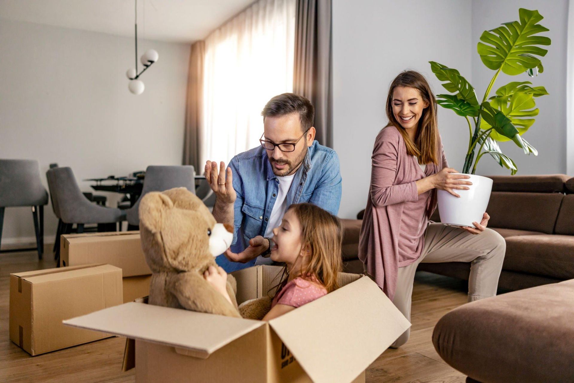 A family is moving into a new home and playing with a teddy bear in a cardboard box.