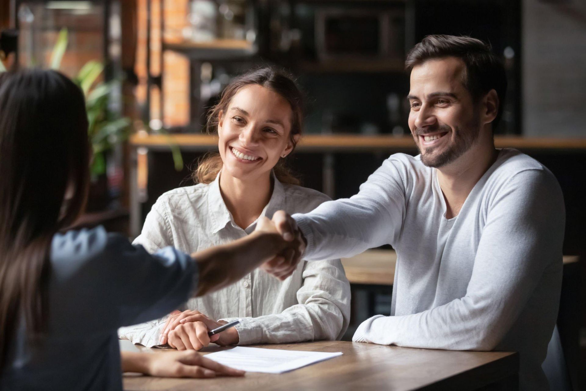 A man and a woman are shaking hands while sitting at a table.