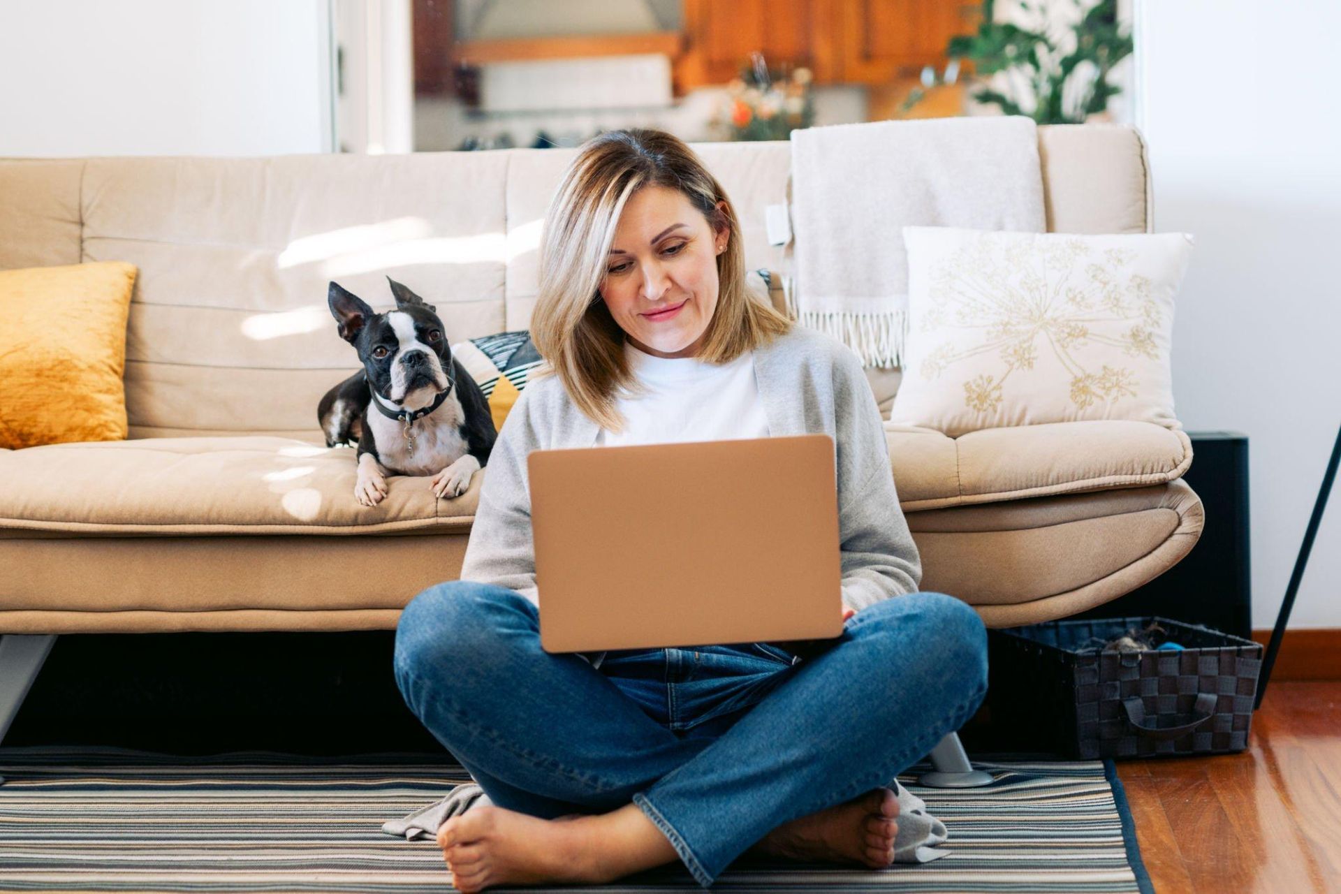 A woman is sitting on the floor using a laptop next to a dog.