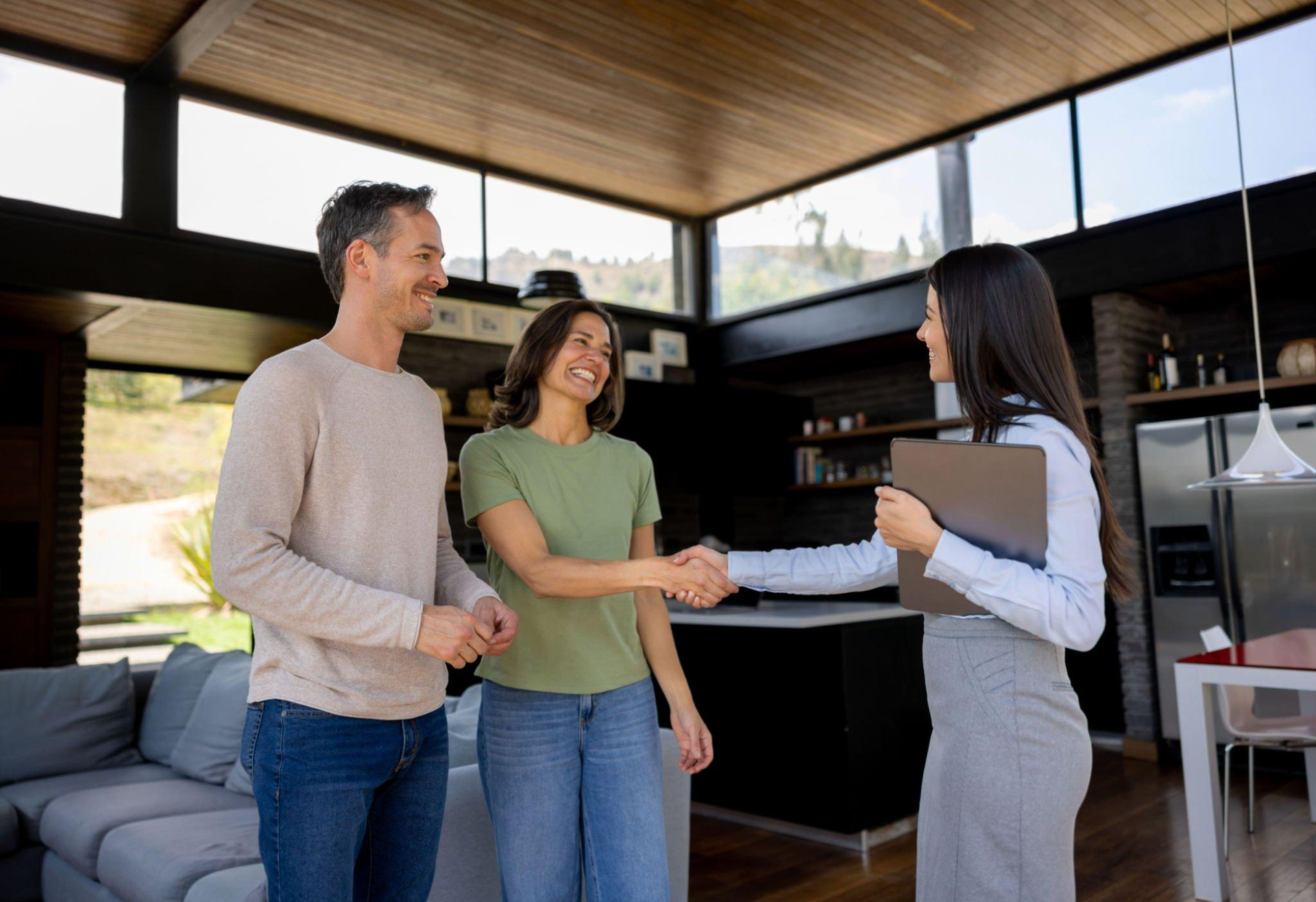 A man and woman are shaking hands with a real estate agent in a living room.