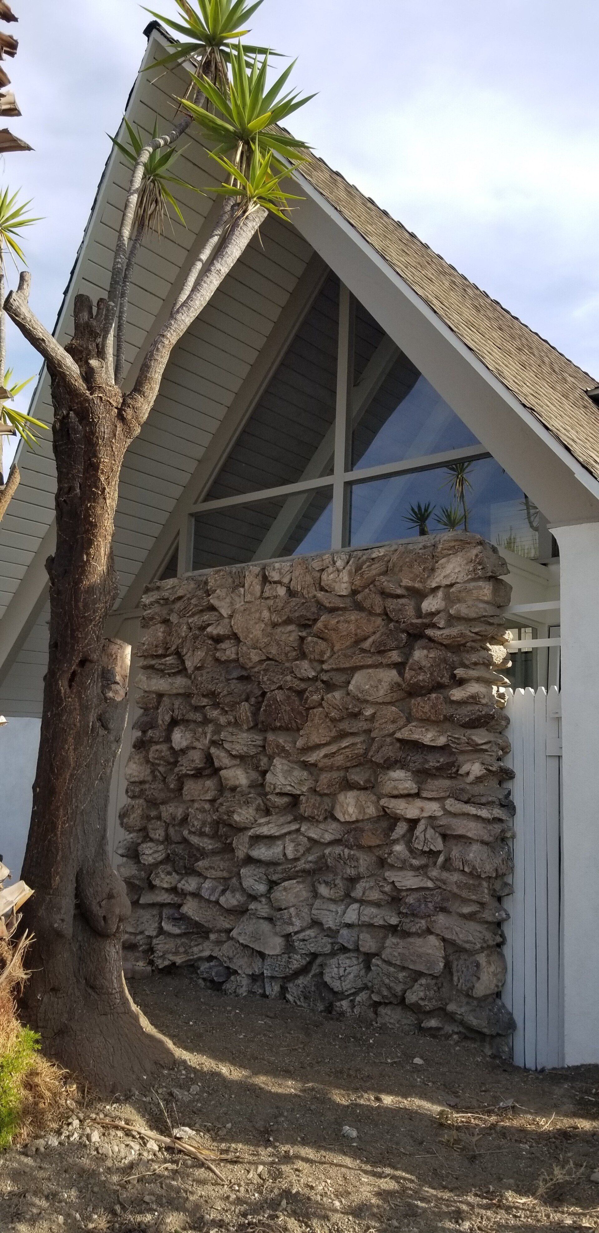 A house with a stone wall and a tree in front of it.