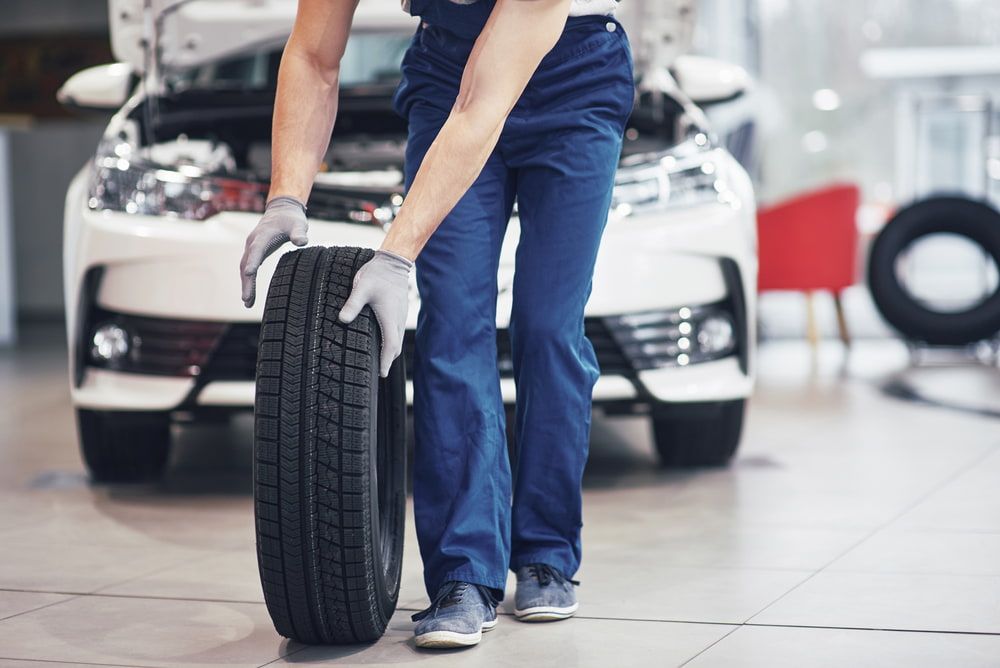 A Man is Holding a Tire in Front of a Car in a Garage — Quick Fix Automotive in Ballina, NSW