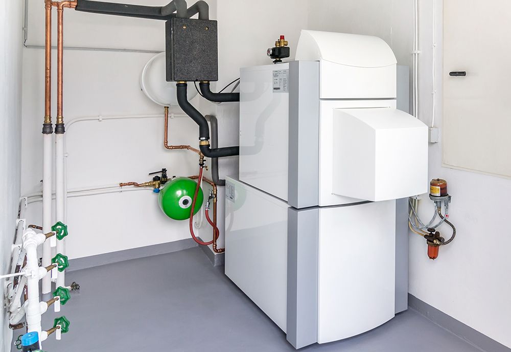 A modern, white and gray boiler unit in a clean utility room with copper pipes, a green pressure tank, and wall valves.