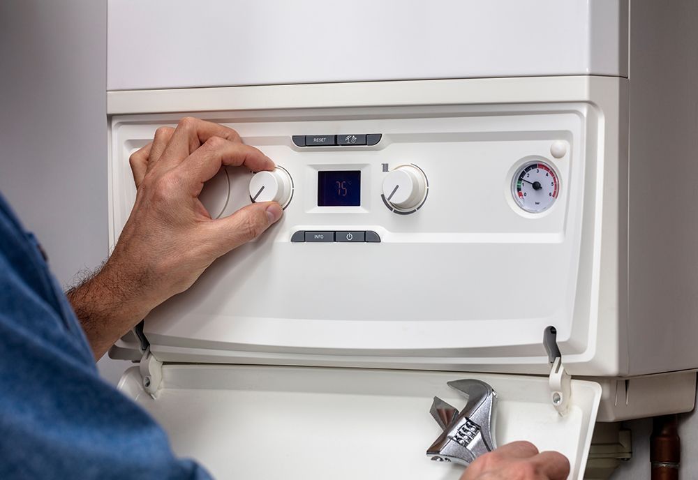 A technician adjusts the dials on a white wall-mounted boiler while holding a wrench.
