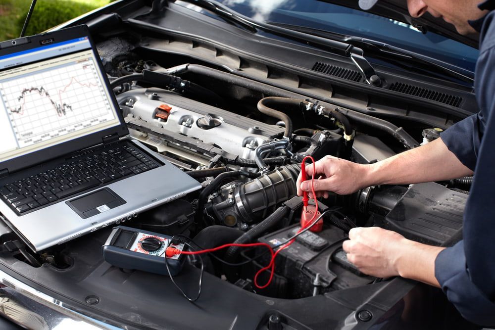 Mechanic Uses a Laptop and Multimeter to Diagnose a Car Engine in a Garage — Autopro Taree in Taree, NSW