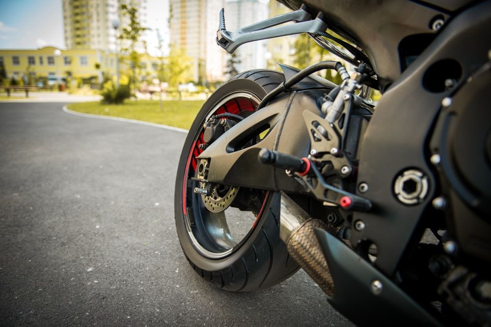 Black Motorcycle Parked on Asphalt, Featuring the Rear Wheel and Exhaust Pipe — Autopro Taree in Taree, NSW