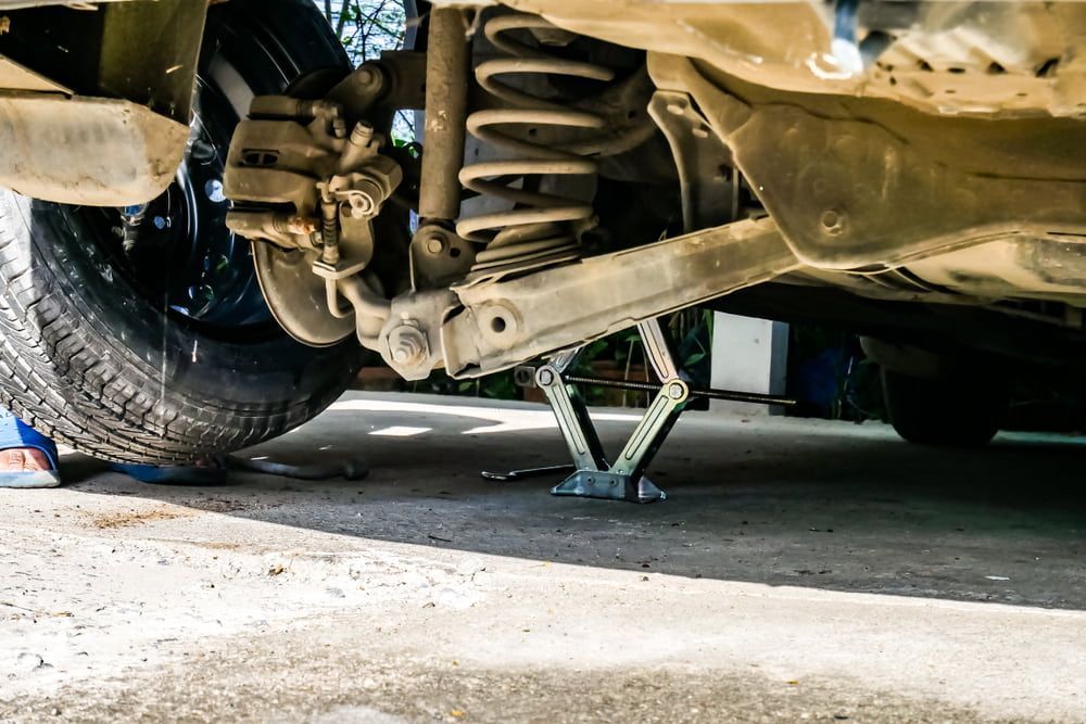 Car Raised on a Jack to Change a Tire. A Flat Tire Rests on the Ground — Autopro Taree in Taree, NSW